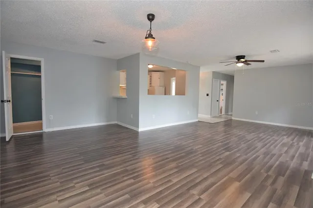 a view of an empty room with wooden floor and a ceiling fan