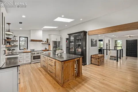 a kitchen with stainless steel appliances kitchen island granite countertop a stove top oven a sink a dining table and chairs with wooden floor