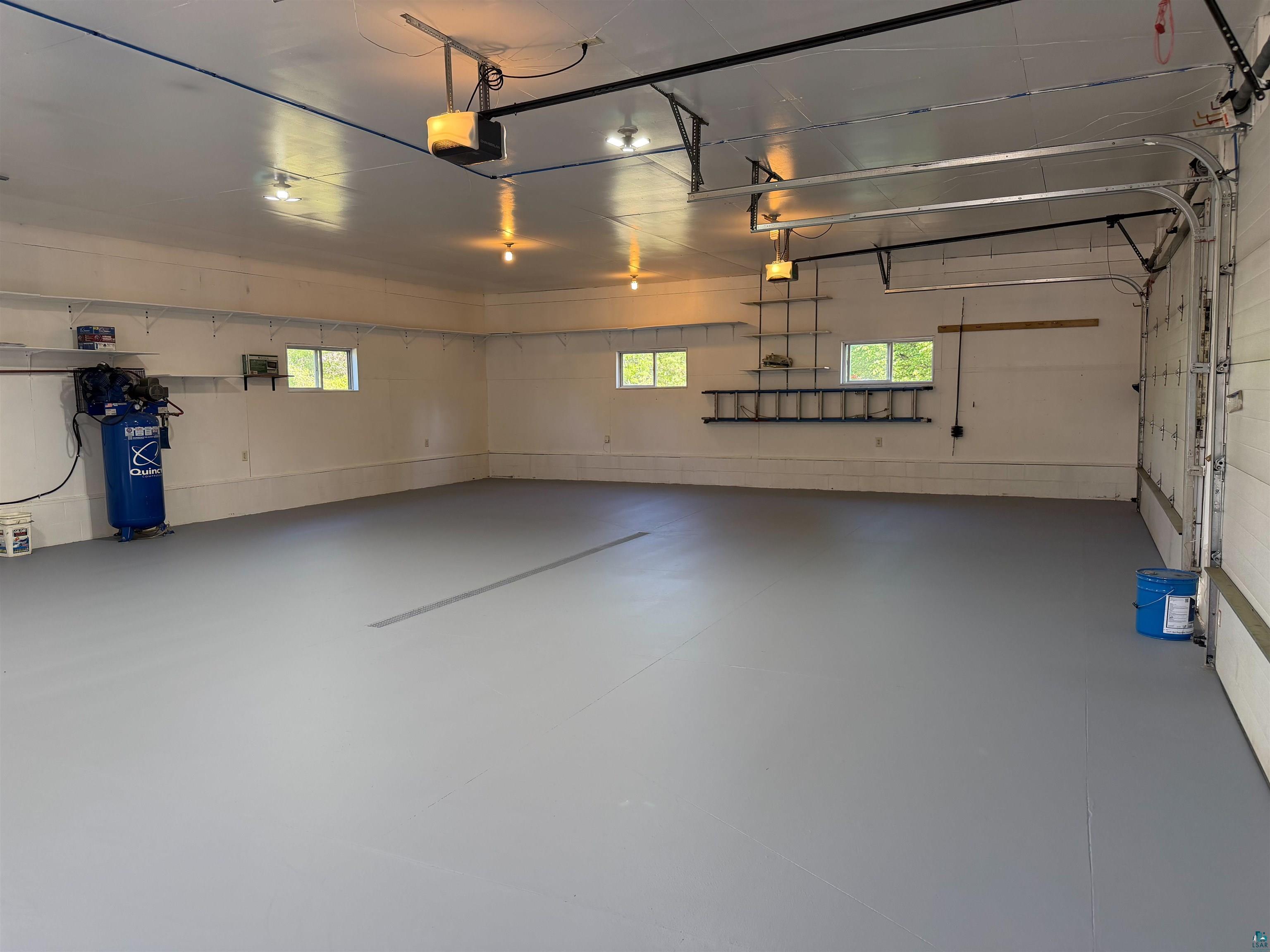 11702 East Mail Road Gordon, WI 54838 - Photo 59 of 60 Spacious garage featuring a durable gray floor coating, multiple windows for natural illumination, exposed ceiling beams, and integrated overhead lighting fixtures