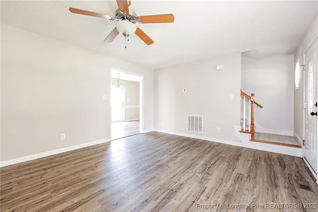 an empty room with wooden floor ceiling fan and windows