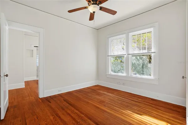 an empty room with wooden floor chandelier fan and windows