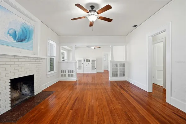 a view of an empty room with wooden floor and a kitchen