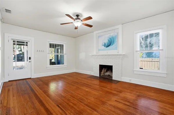 a view of an empty room with wooden floor fireplace and a window