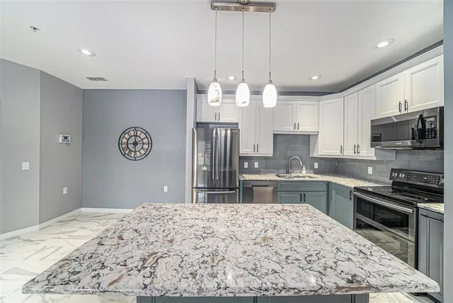a open kitchen with kitchen island granite countertop a stove oven and a sink with cabinets