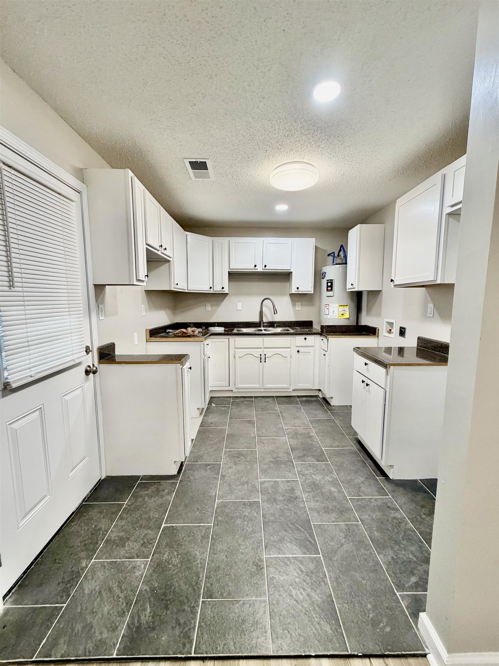 3345 Charlotte Road Memphis, TN 38109 - Photo 10 of 10 Kitchen featuring dark countertops, a textured ceiling, white cabinets, water heater, and recessed lighting