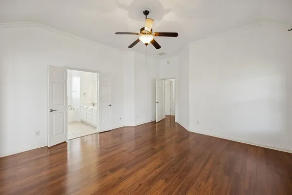 a view of an empty room with wooden floor and a ceiling fan