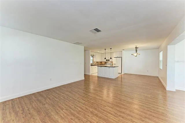 a view of a refrigerator in kitchen and an empty room with wooden floor
