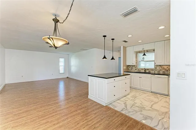 a kitchen with granite countertop a stove a sink and white cabinets with wooden floor