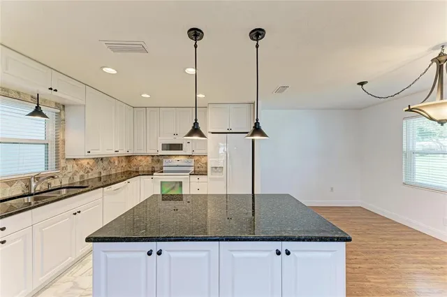 a kitchen with kitchen island granite countertop a sink a counter space appliances and cabinets