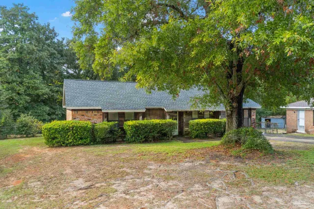 a view of a brick house next to a yard with large trees