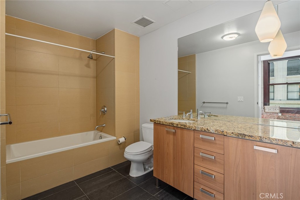 460 South Spring Street, Unit 1013 Los Angeles, CA 90013 - Photo 10 of 25 a bathroom with a granite countertop bathtub shower sink vanity mirror and toilet
