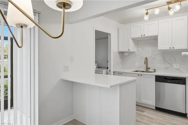 a kitchen with stainless steel appliances a sink dishwasher a refrigerator and white cabinets with wooden floor