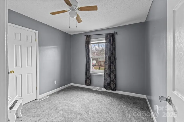 an empty room with chandelier fan and windows