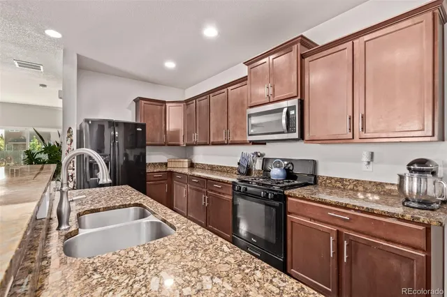 a kitchen with granite countertop a sink a stove top oven a refrigerator cabinets and a counter top space