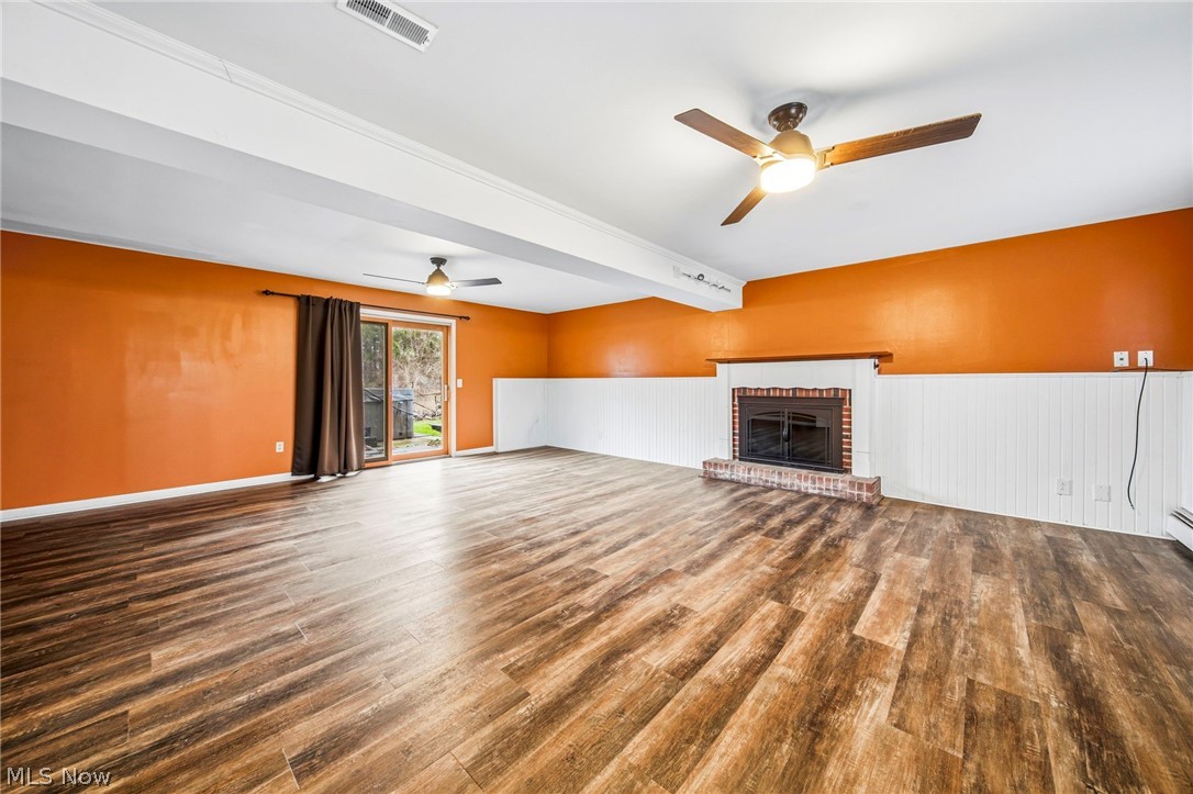 10397 Prouty Road Painesville, OH 44077 - Photo 18 of 32 Unfurnished living room featuring dark wood finished floors, a fireplace, a ceiling fan, and a wainscoted wall