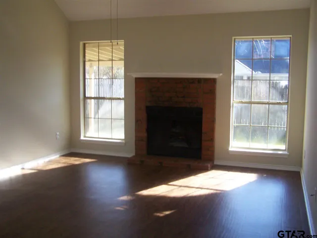 an empty room with wooden floor fireplace and windows