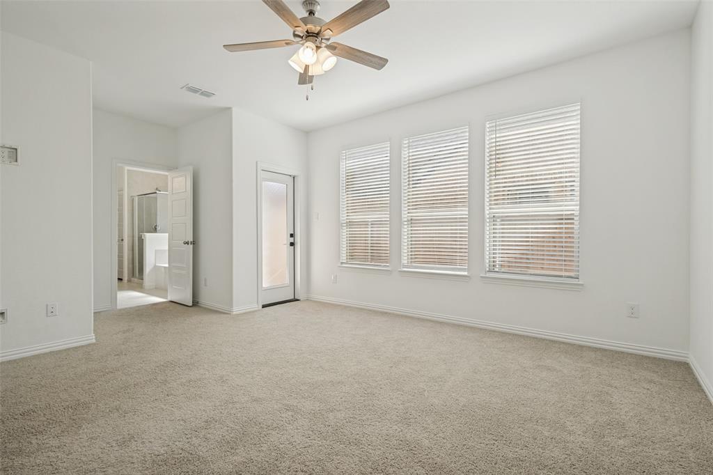 1448 Sun Gdn Way Justin, TX 76247 - Photo 9 of 15 Spacious carpeted room featuring a ceiling fan with light kit, three large windows with blinds, a solid door leading to an outdoor space, and an open doorway to an en-suite bathroom with a glass-enclosed shower