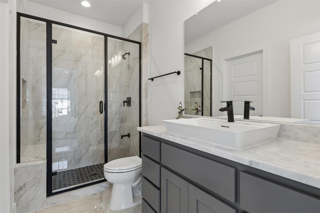 460 Harrison Lane Prosper, TX 75078 - Photo 32 of 40 Curated bathroom featuring a glass-enclosed shower with matte black fixtures, a vessel sink, a stone-finish countertop, and a gray vanity with panel-front cabinetry