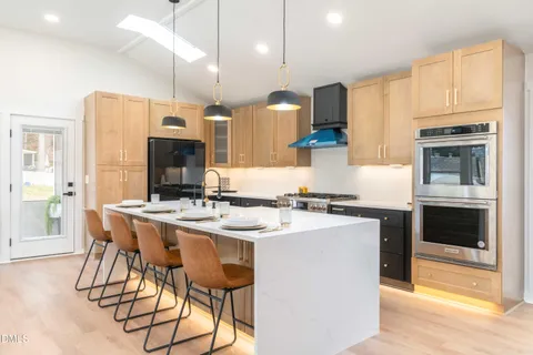 a living room with couches a flat tv screen and kitchen view with wooden floor