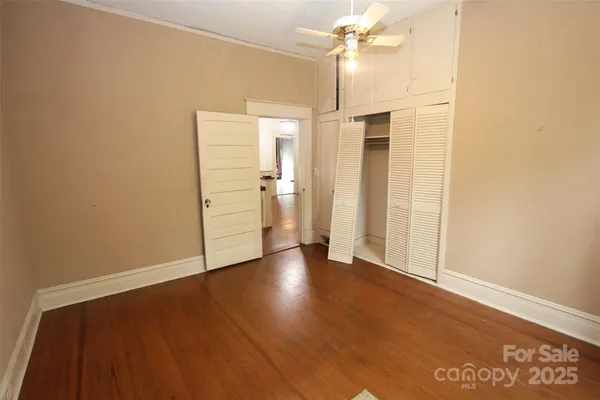 an empty room with wooden floor ceiling fan and window
