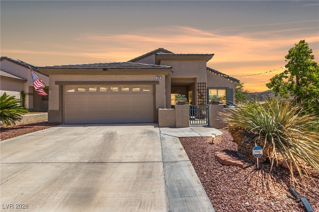 View of front of home featuring a garage, driveway, stucco siding, a gate, and a tile roof