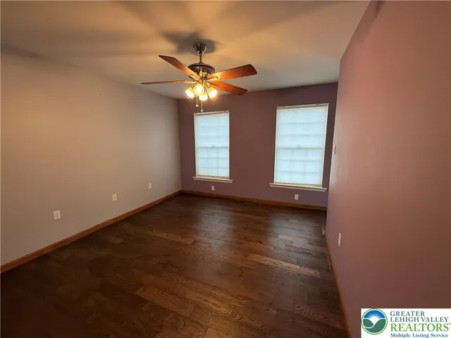 an empty room with wooden floor fan and windows