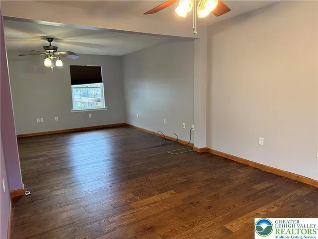 an empty room with wooden floor chandelier fan and windows