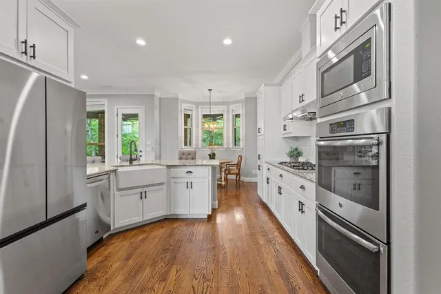 a large kitchen with stainless steel appliances granite countertop a refrigerator a sink dishwasher a oven with white cabinets and wooden floor