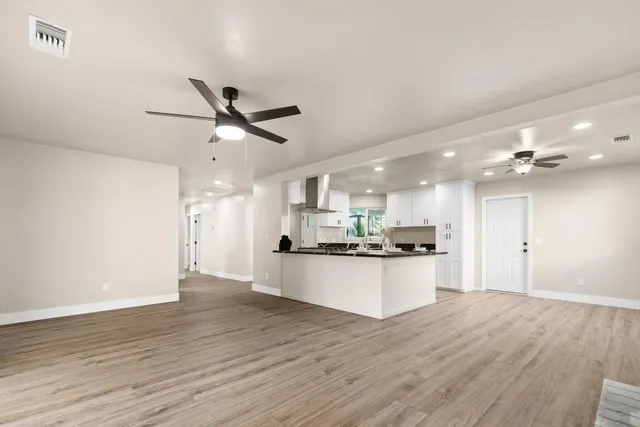 a large kitchen with kitchen island a stove a sink dishwasher a refrigerator and white cabinets with wooden floor