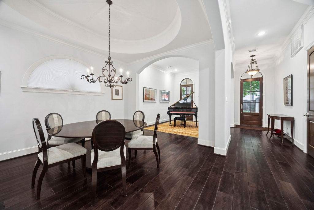 2508 Brun Street Houston, TX 77019 - Photo 11 of 50 This elegant room features dark hardwood floors and a sophisticated chandelier, with a stylish dining area and a grand piano in the adjacent space. Arched windows and doorways add classic charm, and the entryway is inviting with natural light.