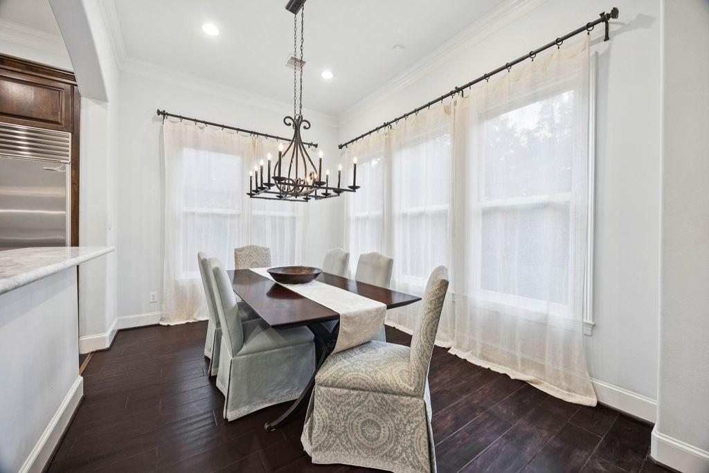 2508 Brun Street Houston, TX 77019 - Photo 13 of 50 Bright dining area with large windows, sheer curtains, and dark wood flooring. Features a stylish chandelier above a wooden table with upholstered chairs, adjacent to a kitchen counter.