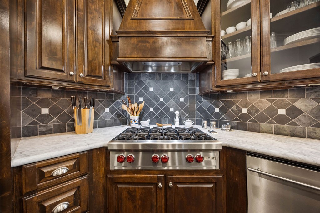 2508 Brun Street Houston, TX 77019 - Photo 15 of 50 This kitchen features hand crafted custom designed cabinetry, a sleek Carrera marble countertop, and a modern stainless steel stove. The backsplash has a stylish geometric tile design, and open shelving displays elegant dishware.