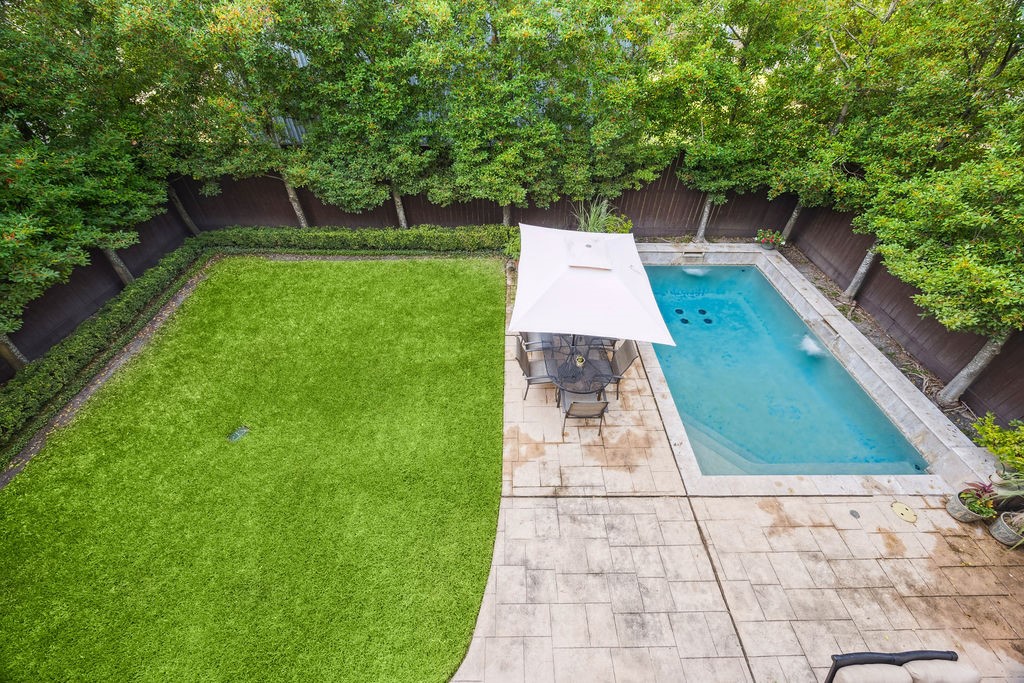2508 Brun Street Houston, TX 77019 - Photo 22 of 50 This backyard features a spacious patio with a dining set under an umbrella, a rectangular swimming pool, and a neatly manicured lawn, all surrounded by mature trees for privacy.