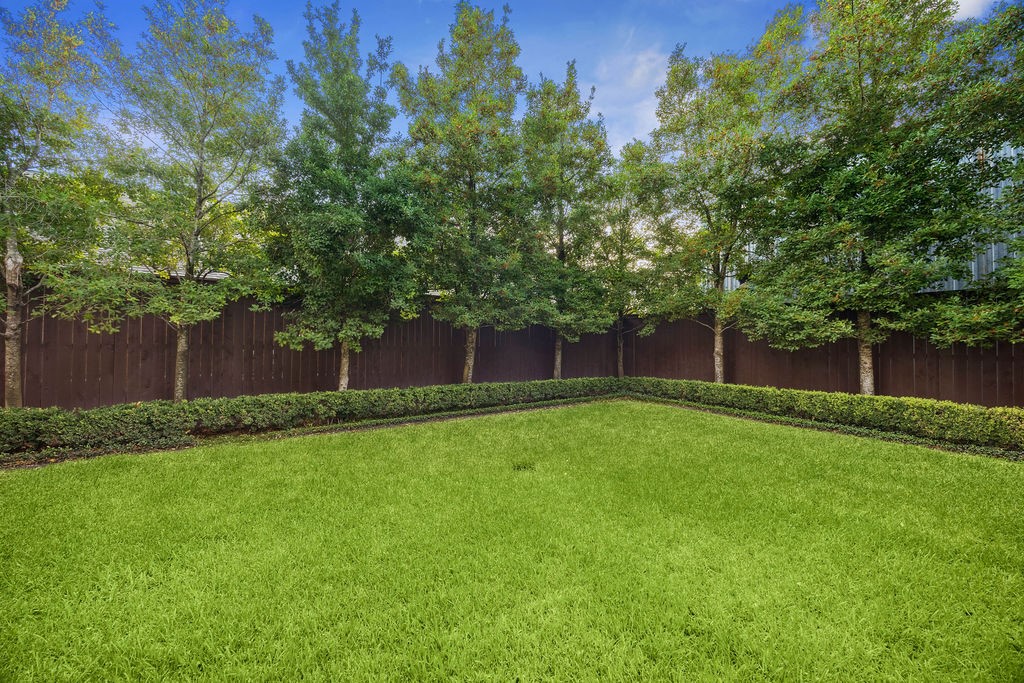 2508 Brun Street Houston, TX 77019 - Photo 24 of 50 A spacious backyard featuring a well-maintained lawn, bordered by small shrubs and a row of tall trees for privacy. It's enclosed by a wooden fence, offering a serene outdoor space.