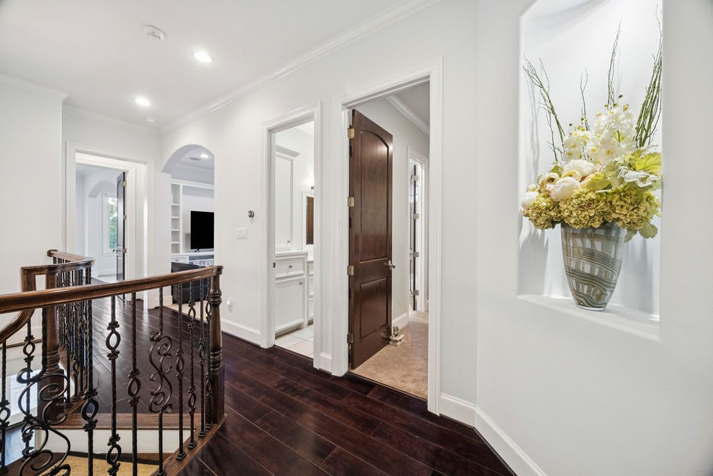 2508 Brun Street Houston, TX 77019 - Photo 26 of 50 At the top of the stairs we have an elegant hallway with dark hardwood floors, decorative railing, and recessed lighting. It features a built-in niche with a large floral arrangement, and offers views into adjacent rooms with white trim and solid wood doors.