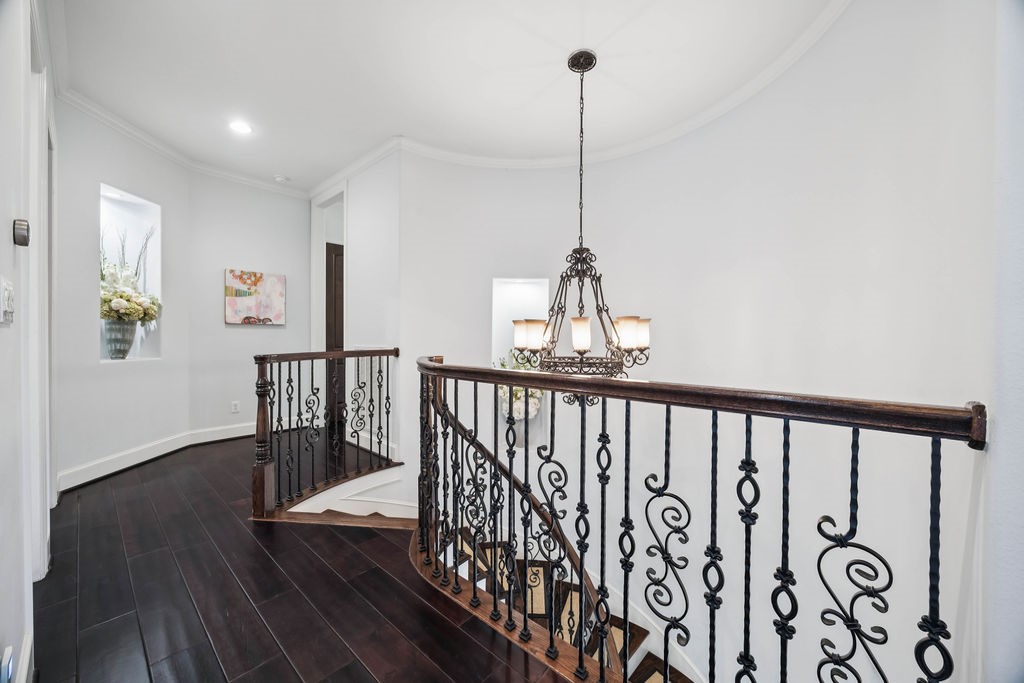 2508 Brun Street Houston, TX 77019 - Photo 27 of 50 This photo showcases an elegant landing area with dark hardwood floors, decorative wrought iron railings, and a stylish chandelier. The curved staircase adds a touch of sophistication, while wall niches with decor enhance the charm.