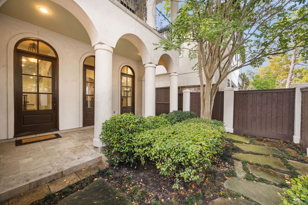 2508 Brun Street Houston, TX 77019 - Photo 3 of 50 This photo showcases an elegant home entrance with arched doorways and pillar accents, leading to a small, landscaped courtyard. The area is enclosed by a tall wooden fence, providing privacy and a touch of nature with lush greenery and a stone path.
