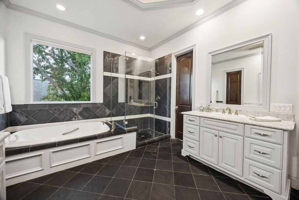 2508 Brun Street Houston, TX 77019 - Photo 33 of 50 This bathroom features a modern, elegant design with a spacious glass-enclosed shower, a luxurious soaking tub, and a large vanity with ample storage. The Travertine tile flooring accents contrast beautifully with the white cabinetry and walls, creating a sophisticated atmosphere. Natural light streams in through a window, enhancing the space.