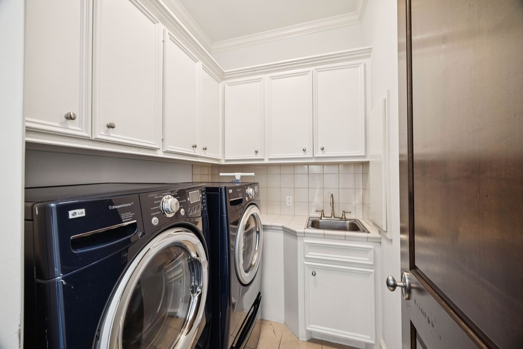 2508 Brun Street Houston, TX 77019 - Photo 36 of 50 This photo shows a compact laundry room featuring a modern washer and dryer set. It includes white cabinetry for storage and a utility sink, providing both functionality and convenience. This utility can be accessed from one of the primary closets.