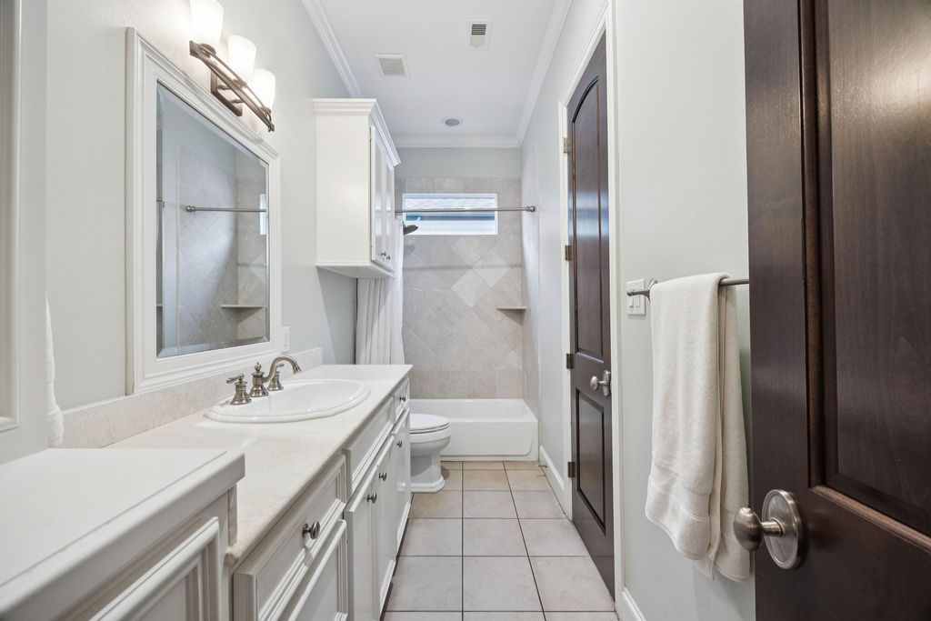 2508 Brun Street Houston, TX 77019 - Photo 39 of 50 This bathroom features a clean, bright design with white cabinetry and light tiles. It includes a single sink vanity, a large mirror, and a combined shower and bathtub. A window above the tub provides natural light, and a solid wooden door adds a touch of warmth.