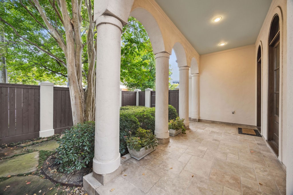 2508 Brun Street Houston, TX 77019 - Photo 4 of 50 This inviting home features a charming covered patio with elegant arches and Travertine tile flooring, surrounded by a privacy fence and lush greenery, creating a serene outdoor space.