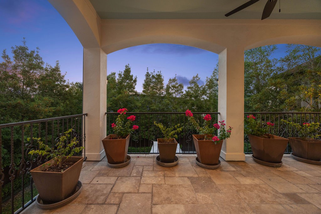 2508 Brun Street Houston, TX 77019 - Photo 44 of 50 This photo showcases a spacious outdoor patio with elegant tile flooring and a wrought iron railing. The area is adorned with potted plants and flowers, providing a serene view of lush greenery under a twilight sky. Ideal for relaxation or entertaining.