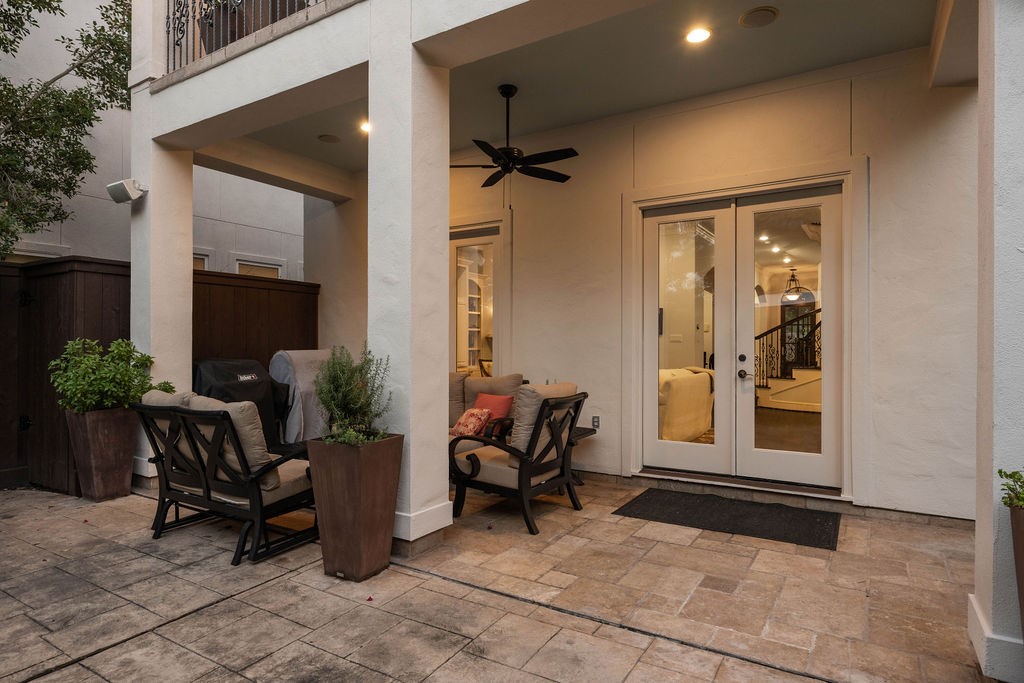 2508 Brun Street Houston, TX 77019 - Photo 45 of 50 This photo showcases a cozy outdoor patio with comfortable seating, a ceiling fan, and potted plants. It leads to the interior through elegant double French doors, offering a glimpse of a warm, inviting living space inside.