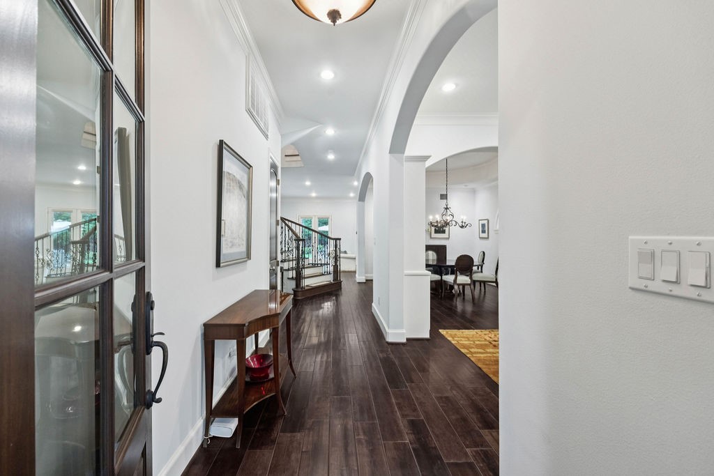 2508 Brun Street Houston, TX 77019 - Photo 5 of 50 This photo showcases a bright, spacious entryway with elegant dark wood flooring, leading into an open-concept living area. The hallway features a stylish light fixture and decorative arches, enhancing the home's sophisticated design.