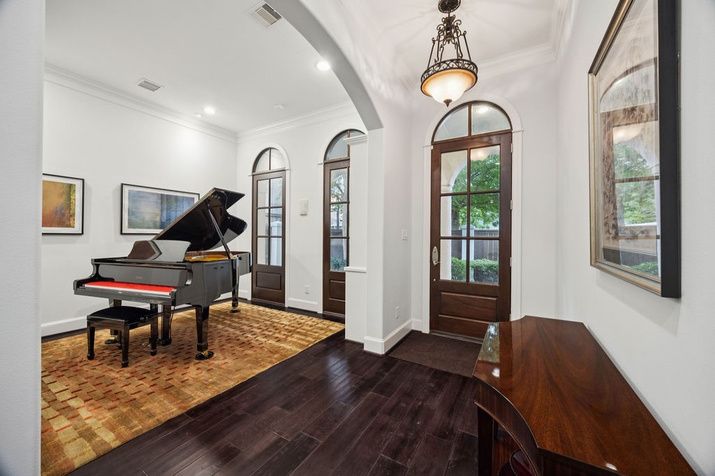 2508 Brun Street Houston, TX 77019 - Photo 6 of 50 This elegant room features dark hardwood flooring, a grand piano, and high ceilings with recessed lighting. Arched windows and a solid wooden door add charm, while the neutral walls and modern artwork create a sophisticated atmosphere.
