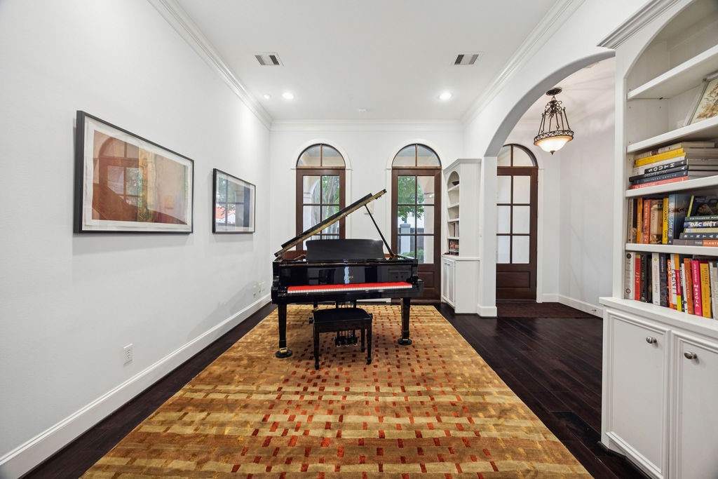 2508 Brun Street Houston, TX 77019 - Photo 7 of 50 This elegant room features a grand piano, surrounded by dark hardwood floors. It includes arched windows and doorways, built-in bookshelves, creating a sophisticated and inviting atmosphere.