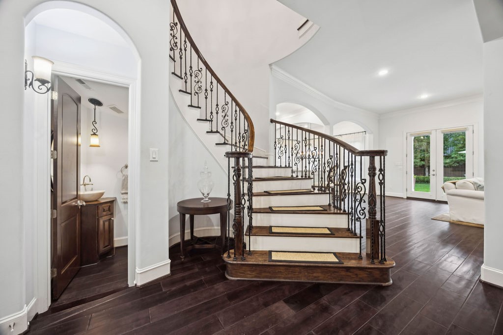 2508 Brun Street Houston, TX 77019 - Photo 8 of 50 This elegant home features a stunning curved staircase with ornate iron railings, hardwood floors, and a cozy living area with large windows opening to a lush backyard. A stylish powder room is conveniently located nearby.