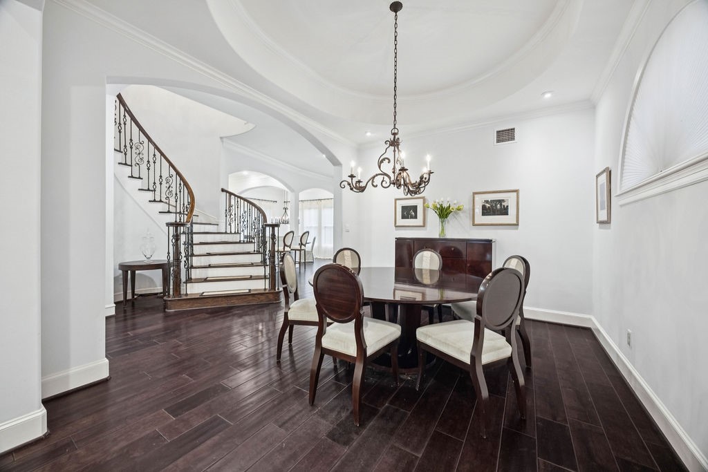 2508 Brun Street Houston, TX 77019 - Photo 9 of 50 This elegant dining area features dark hardwood floors and a stylish chandelier. It's adjacent to a grand staircase with wrought iron railings, creating an open and sophisticated atmosphere.