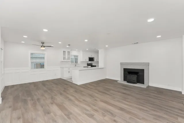 a view of an empty room with kitchen and fireplace