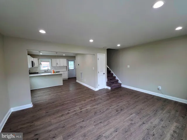 a view of an empty room with wooden floor and a kitchen